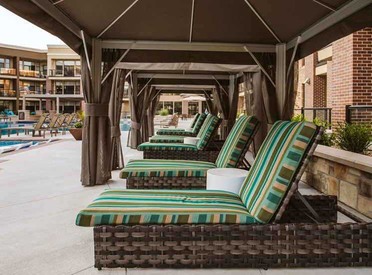 chaise lounge chairs in a row under a canopy next to an outdoor pool